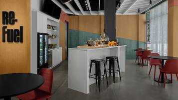 A modern cafe with a central island, red chairs, and a refrigerator.