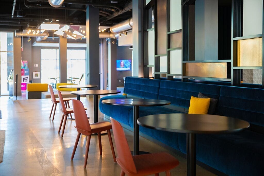 A modern restaurant with blue seating, orange chairs, and round tables.