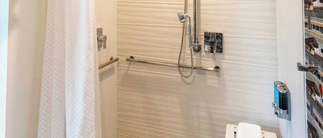A modern bathroom with a glass shower enclosure, a towel rack, and a small shelf with toiletries.