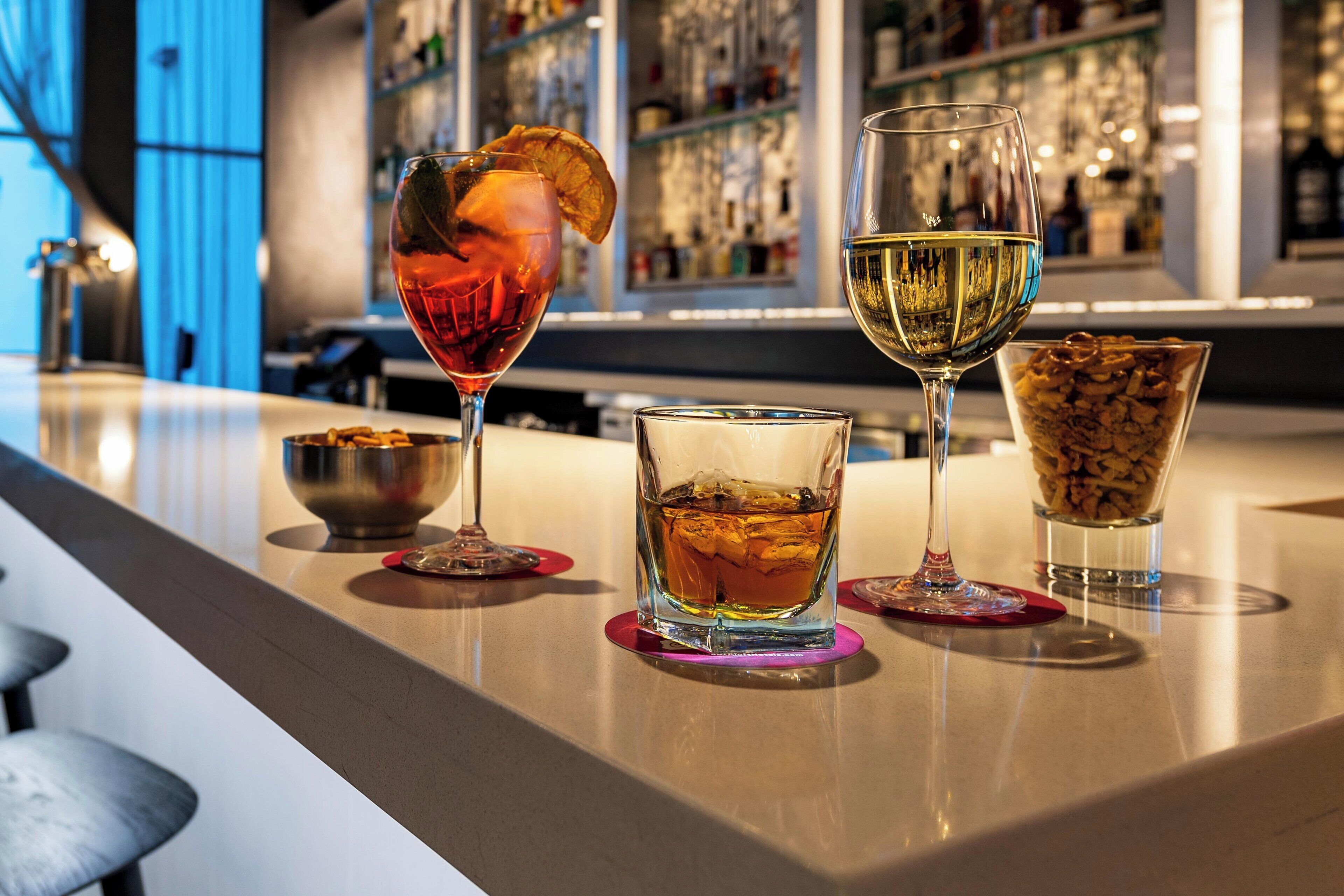 A bar area with three glasses of different beverages, a bowl of nuts, and a bar counter.