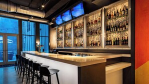 A bar area with a long counter, multiple stools, and shelves of bottles. - Aloft by Marriott Savannah Downtown Historic District (Savannah)