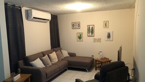 Sala de estar com sofá seccional, uma pequena mesa de madeira, televisão e obras de arte nas paredes.