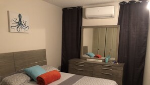 Quarto com cama, cômoda, espelho e ar condicionado.