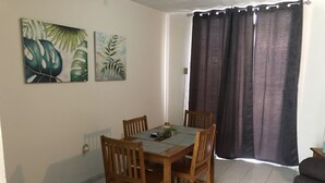 Uma área de refeições com uma mesa de madeira e quatro cadeiras, uma pequena planta e duas pinturas penduradas na parede.
