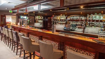 Uma área de bar com um balcão comprido, vários bancos e uma variedade de garrafas e copos.