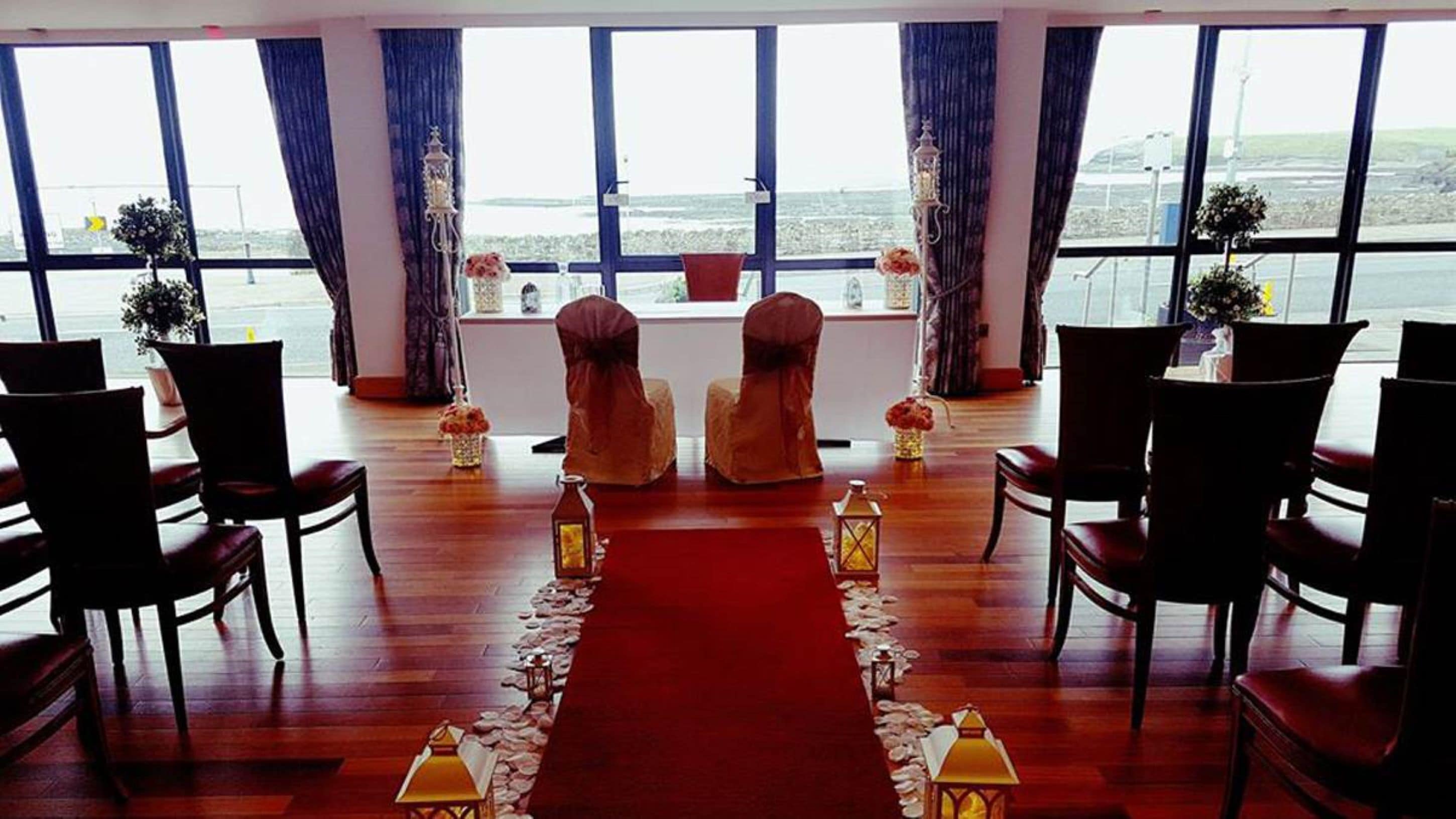 A room with a wooden floor, a red carpet leading to a window, and chairs arranged for a ceremony.