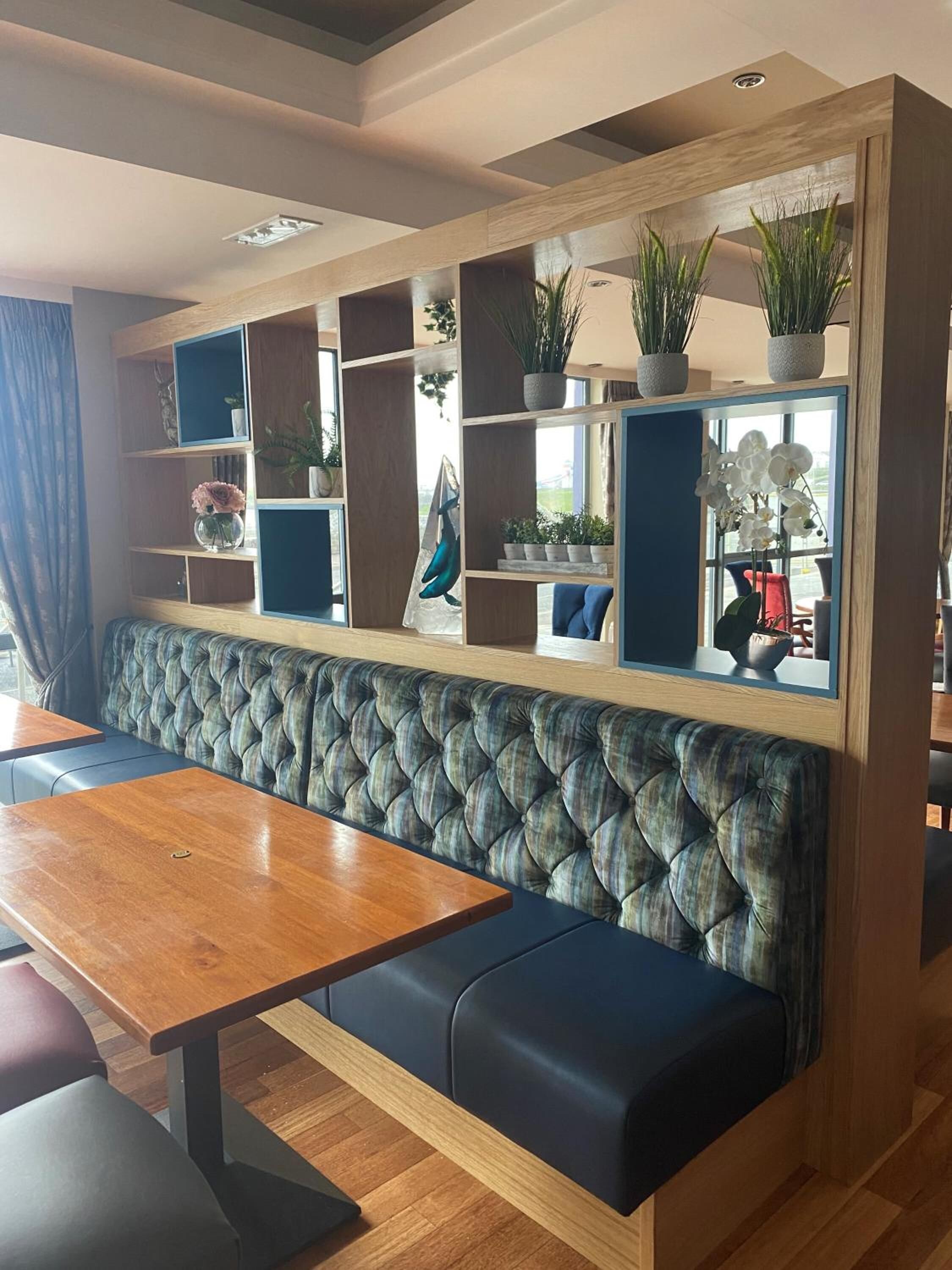 A seating area with a tufted bench and a wooden table, surrounded by shelves with plants and decorative items.