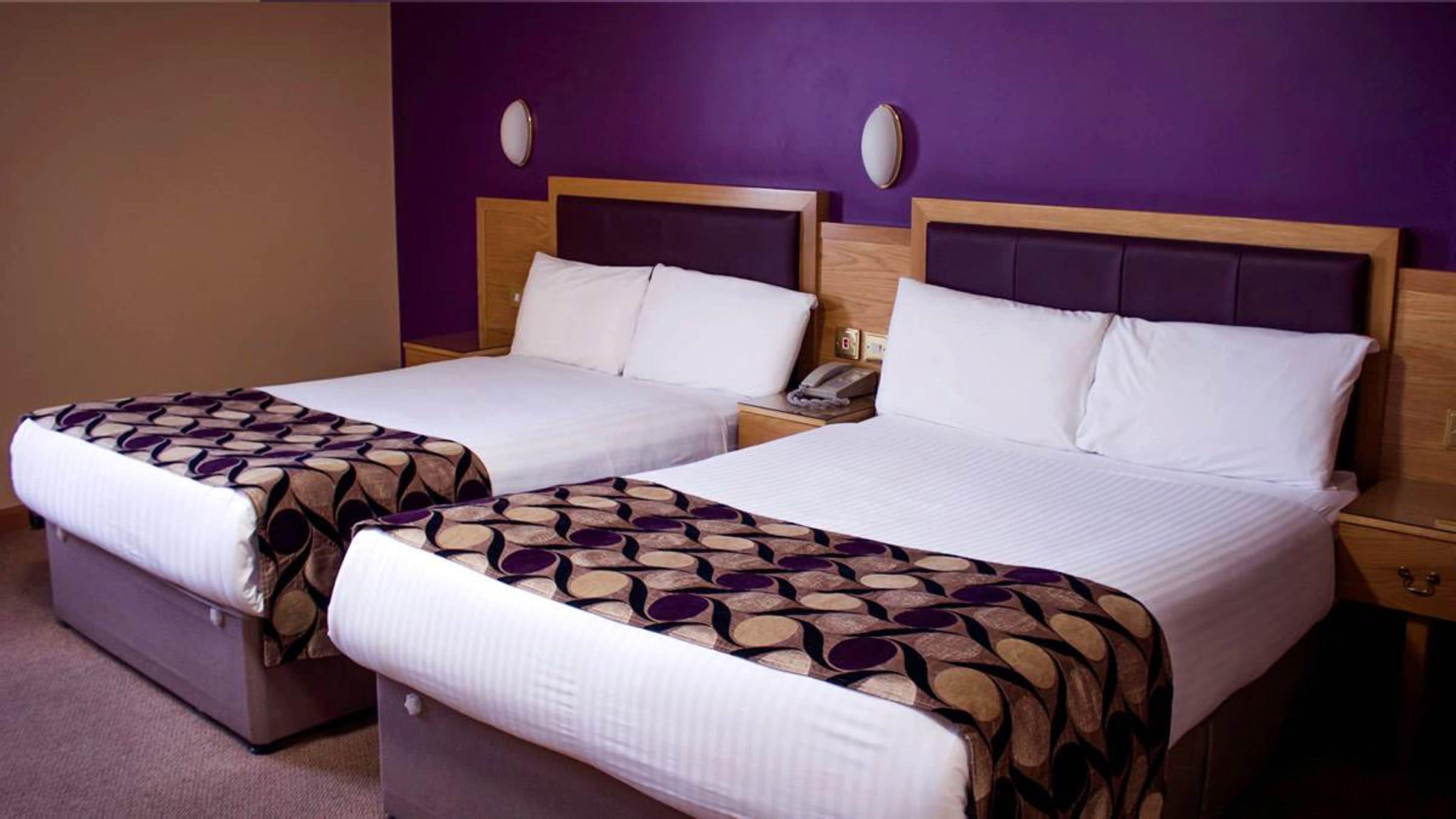 Two single beds with headboards, a bedside table with a phone, and a wall-mounted light fixture.