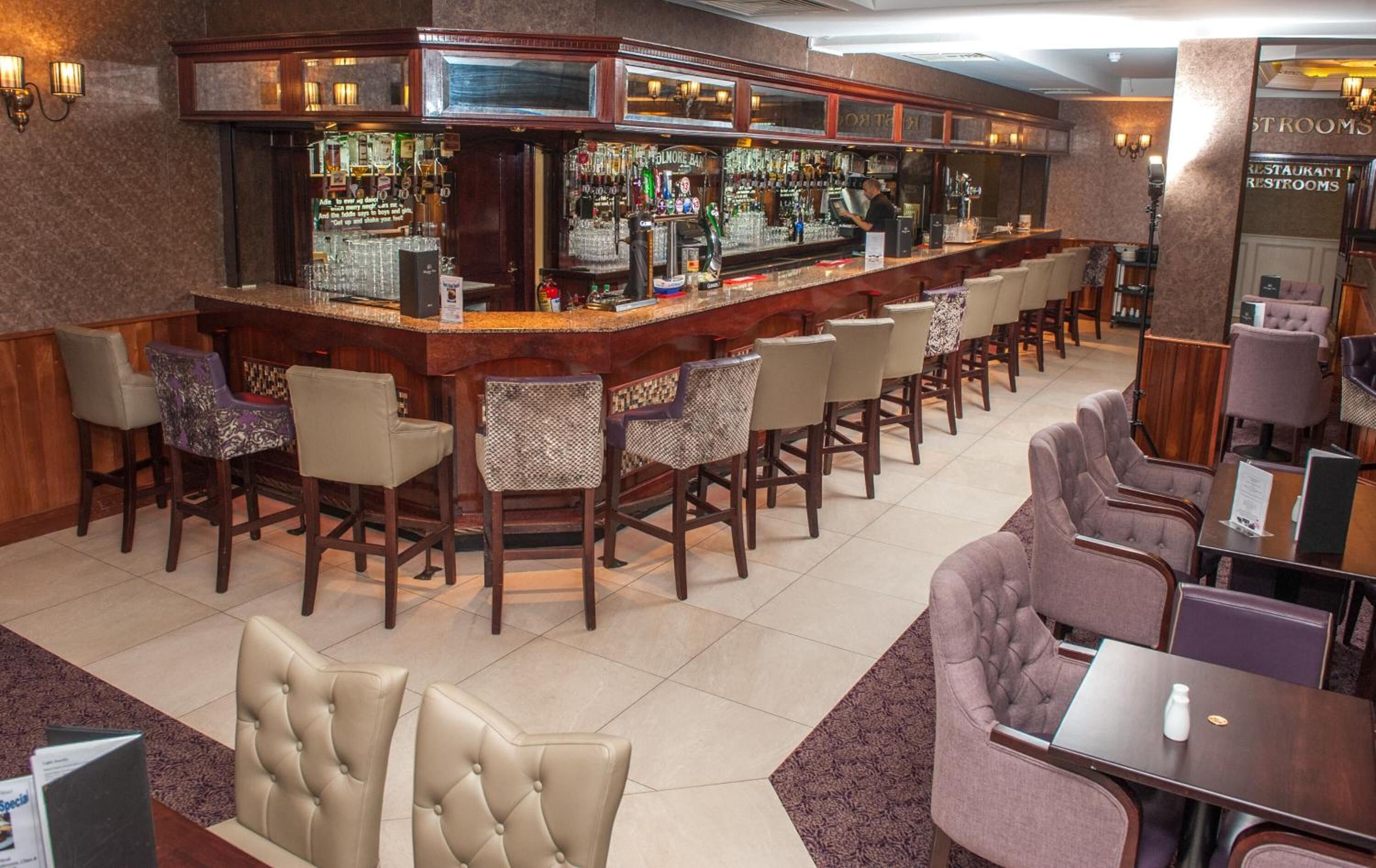 A bar area with a counter, bar stools, and a seating area with cushioned chairs.