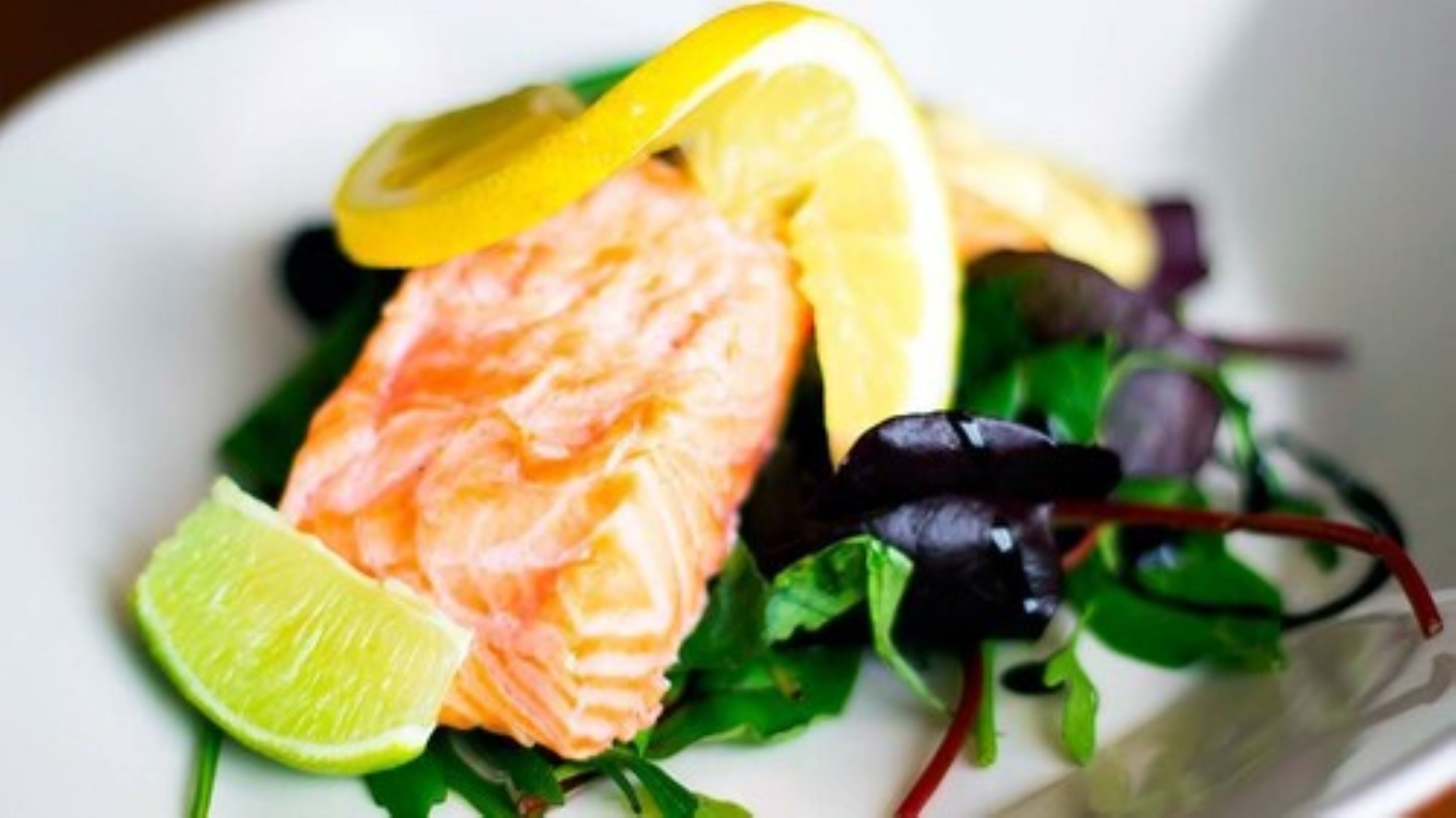 A plate with salmon, lemon slices, and greens.