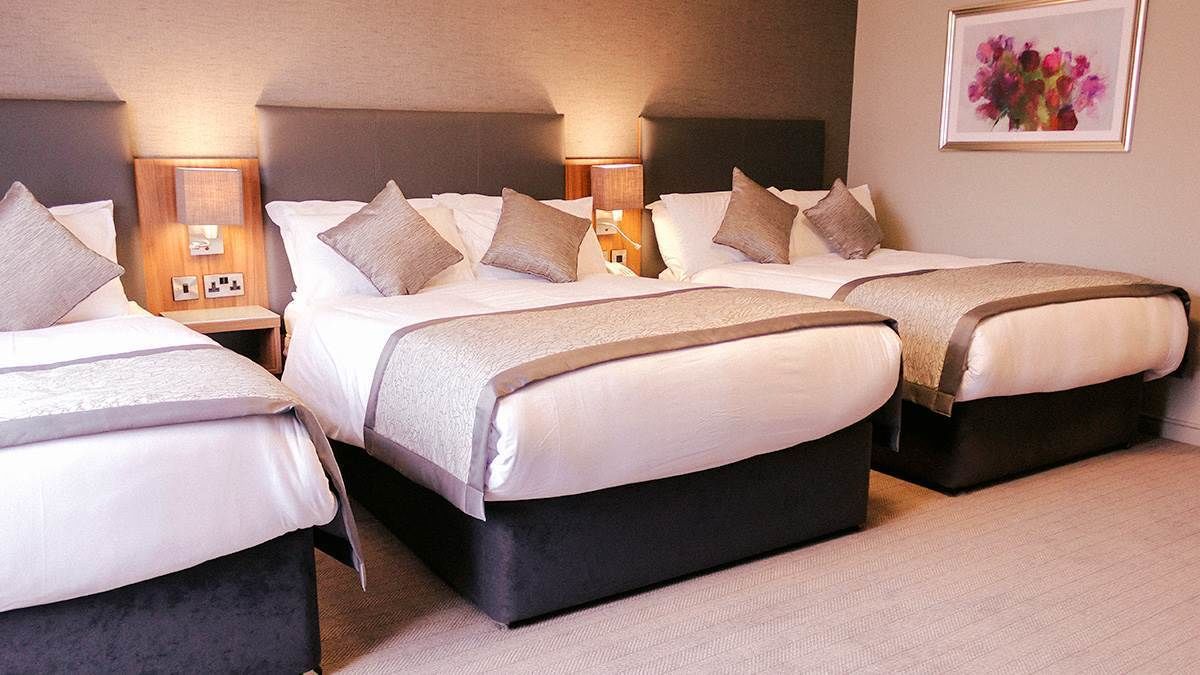 Habitación de hotel con tres camas, cada una con cabecera, mesitas de noche y lámparas.