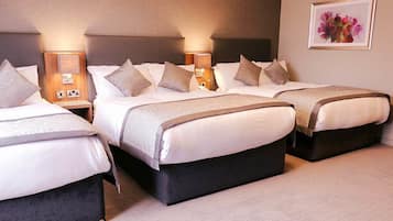 Habitación de hotel con tres camas, cada una con cabecera, mesitas de noche y lámparas.