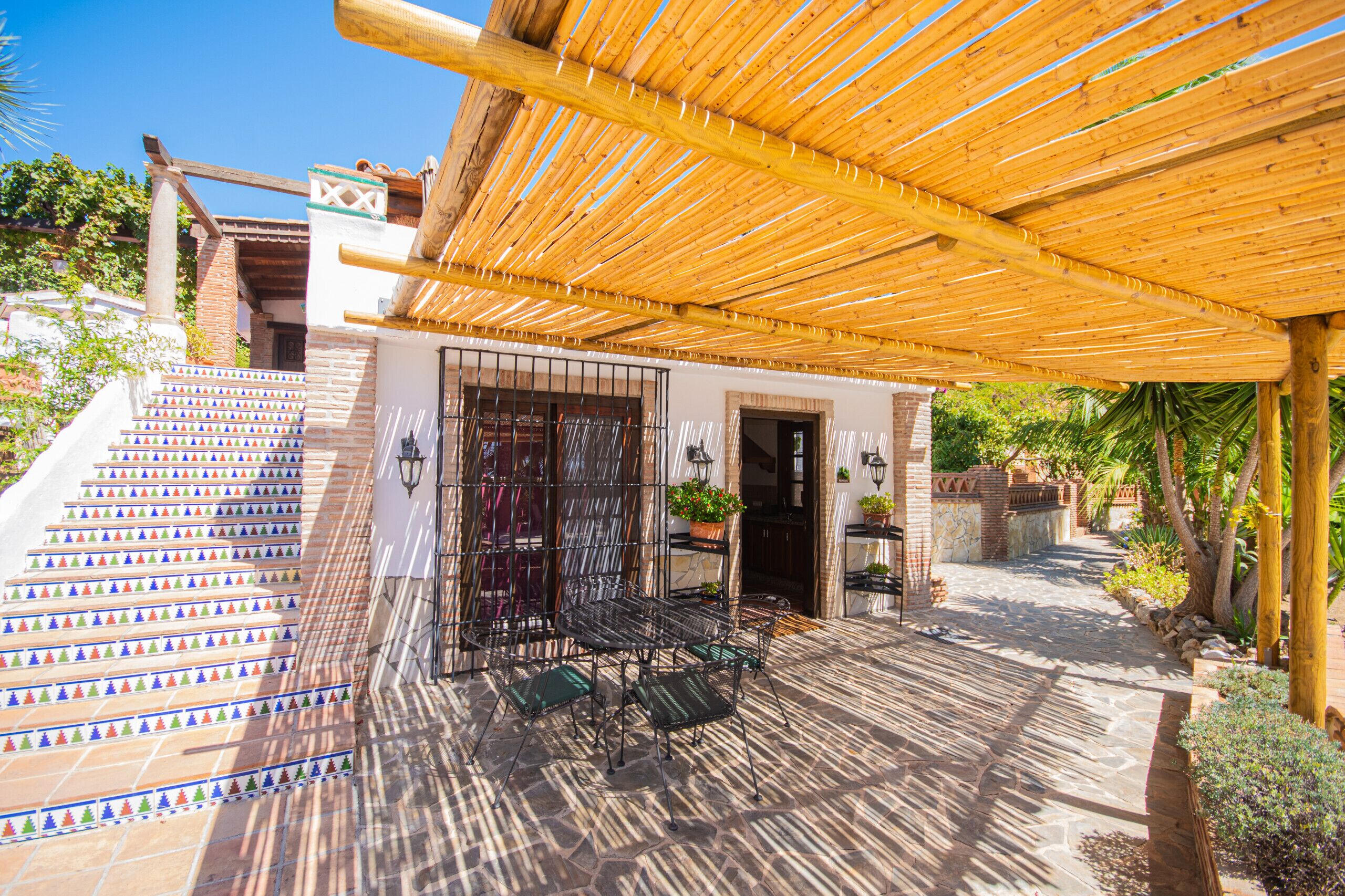 A covered patio area with a wooden pergola, a staircase with colorful triangular tiles, and outdoor furniture.