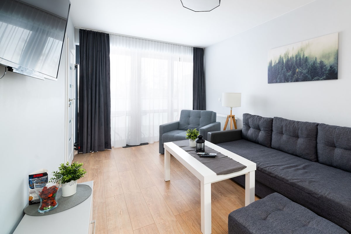 Una sala de estar moderna con un sofá gris, una mesa de centro blanca y un televisor montado en la pared.