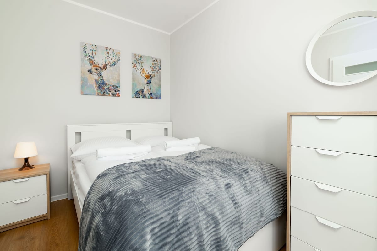 Un dormitorio con cama, mesita de noche, cómoda y dos cuadros colgados en la pared.