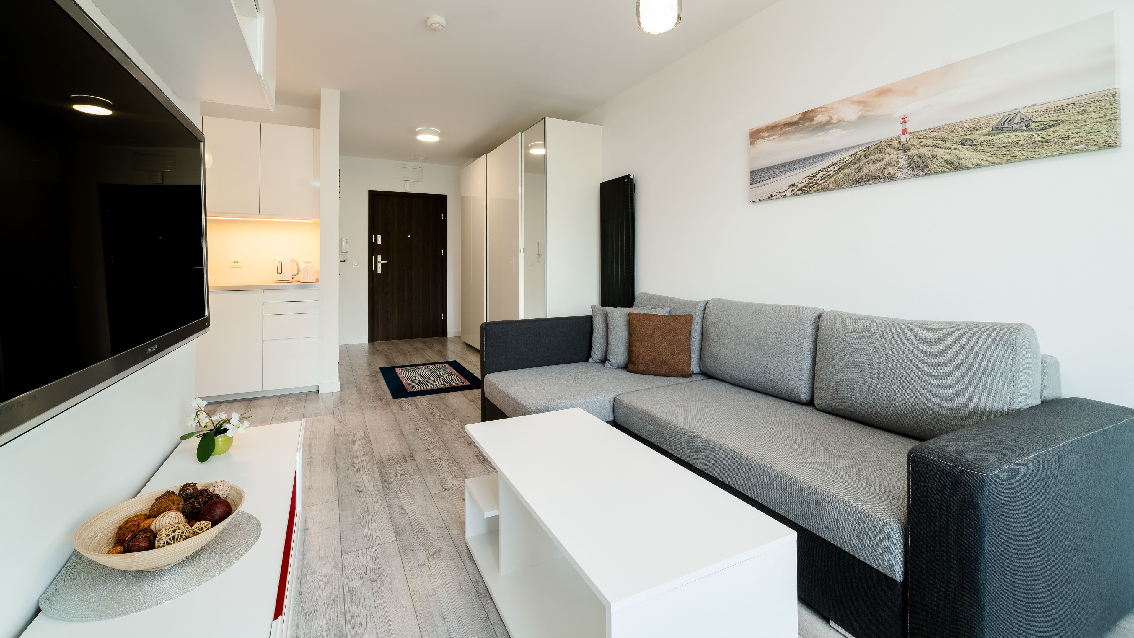 Una sala de estar moderna con un sofá gris, una mesita de centro blanca y un televisor de pantalla plana.