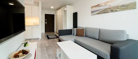 Una sala de estar moderna con un sofá gris, una mesita de centro blanca y un televisor de pantalla plana.