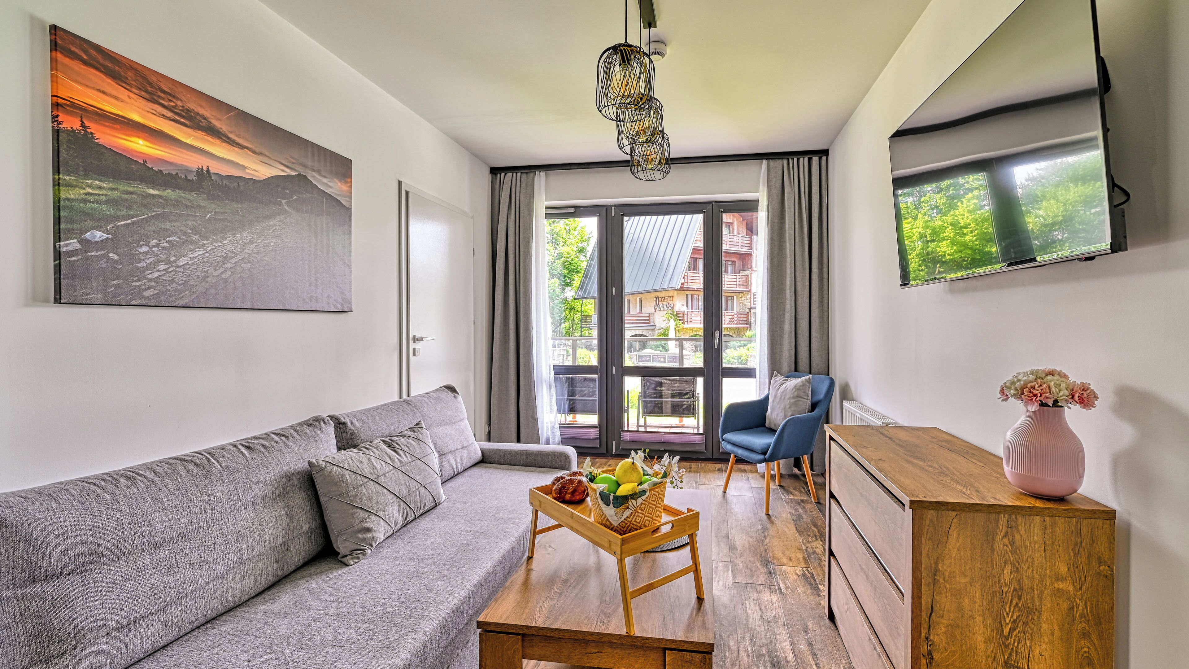 A modern living room with a gray sofa, a wooden coffee table with fruits, a blue armchair, and a wooden cabinet.
