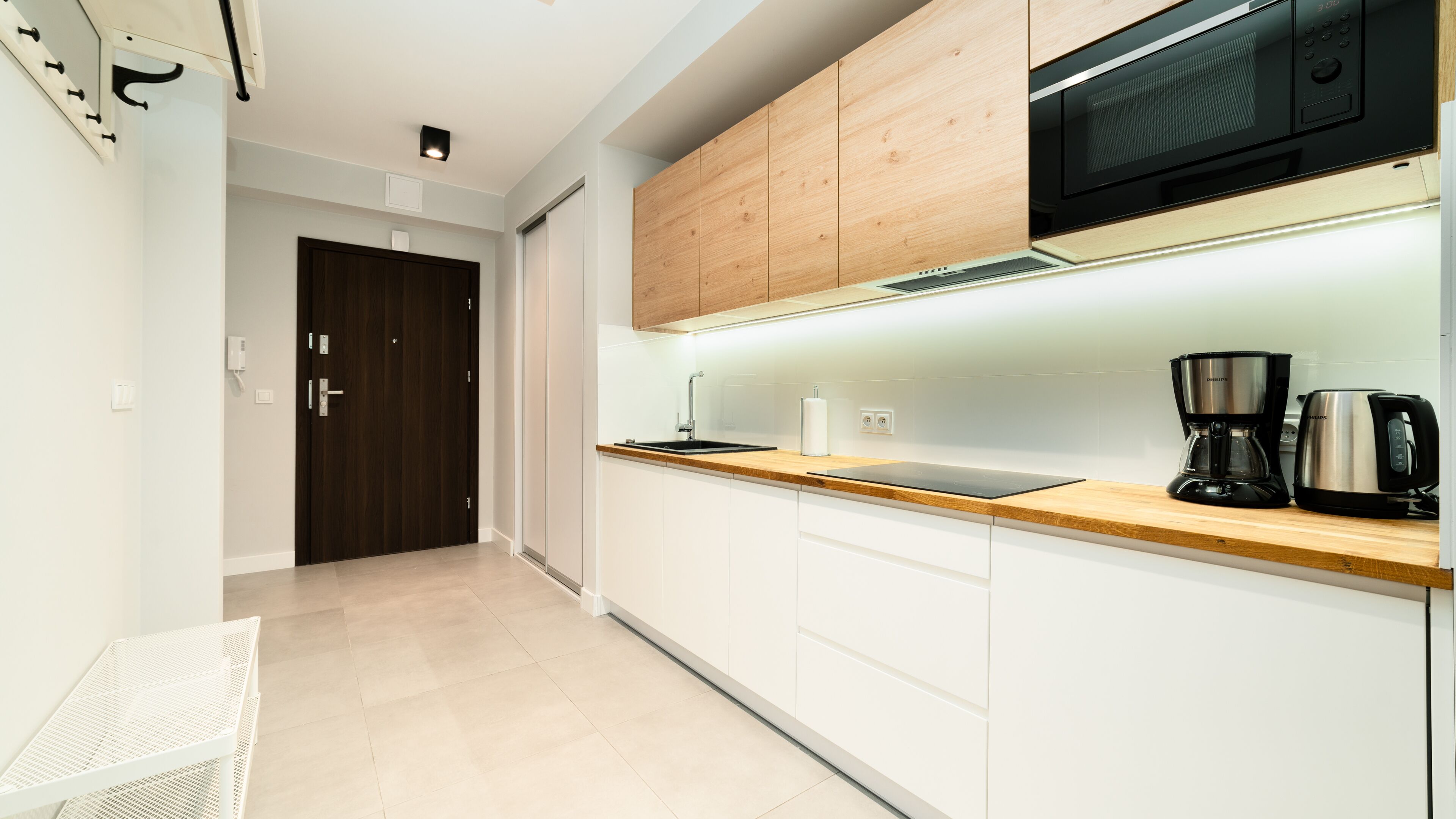 Une cuisine moderne avec des meubles en bois, un micro-ondes noir, une machine à café et un évier.