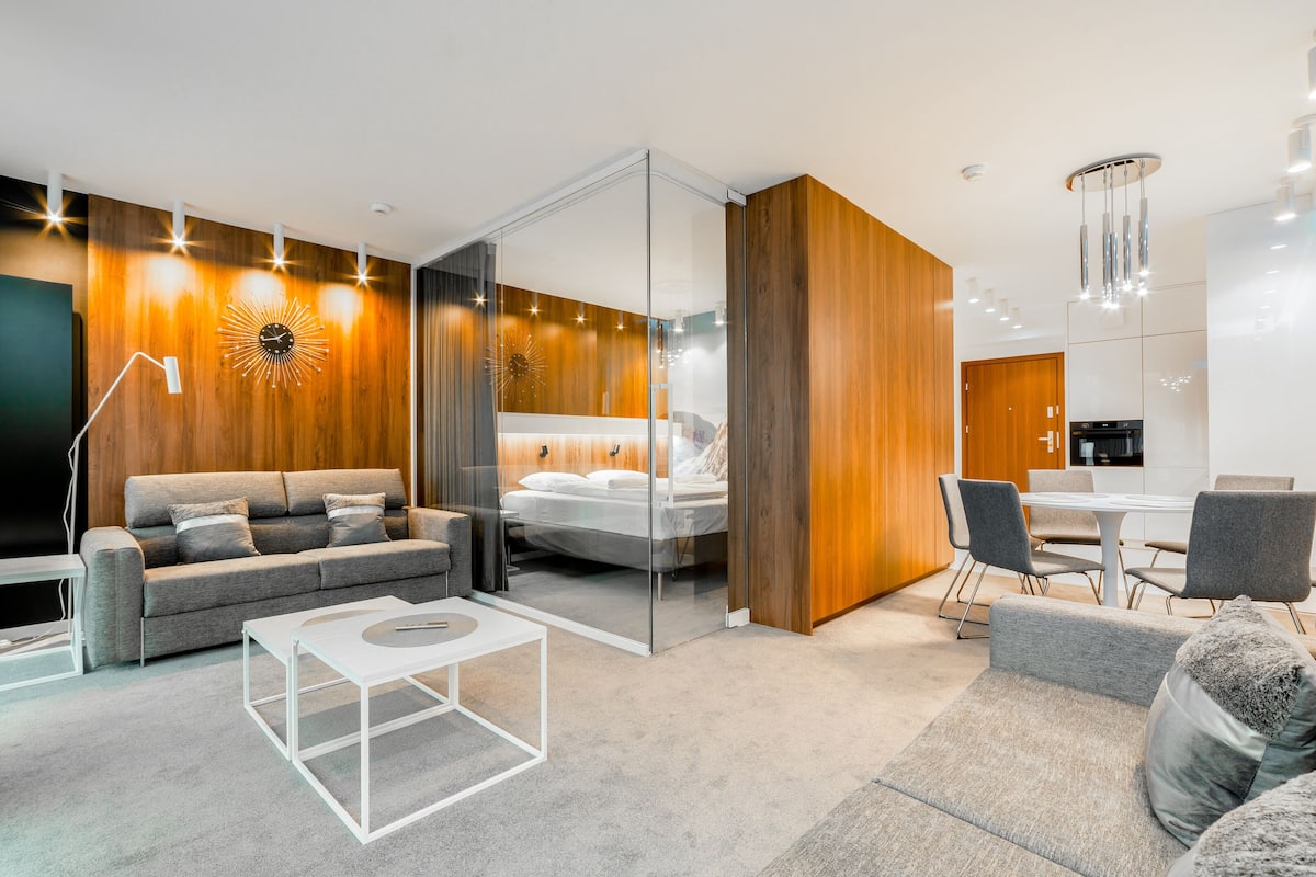 Una habitación de hotel moderna con sofá, cama, zona de comedor y un espejo grande.