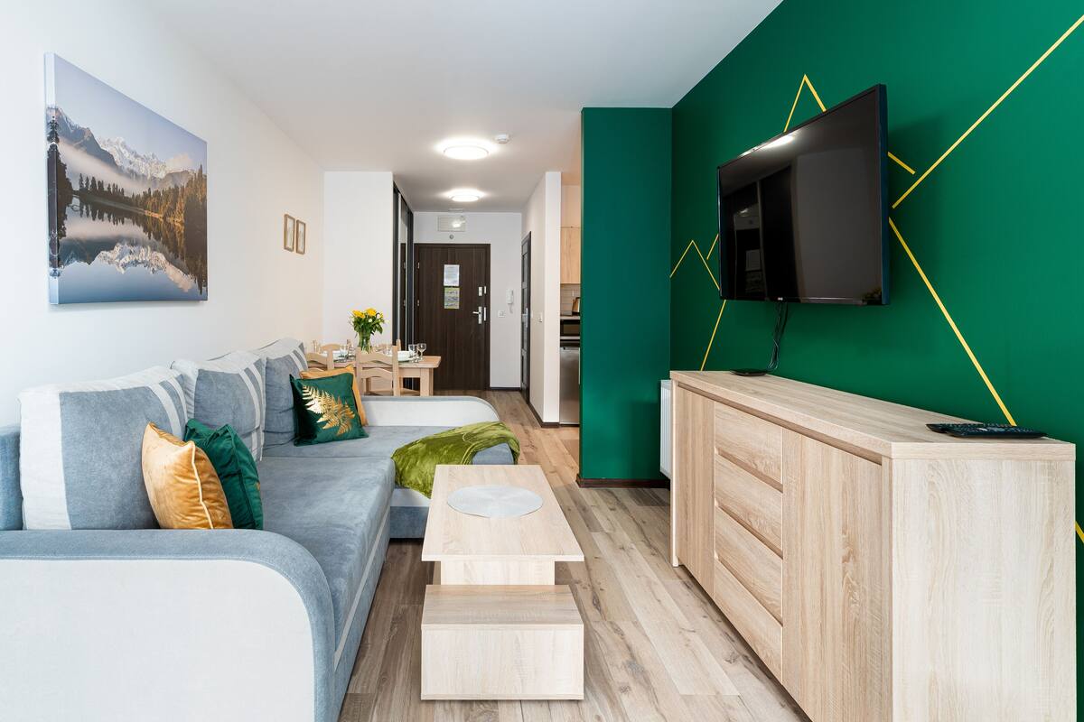 Una sala de estar moderna con un sofá, una mesa de centro y un televisor montado en una pared verde.