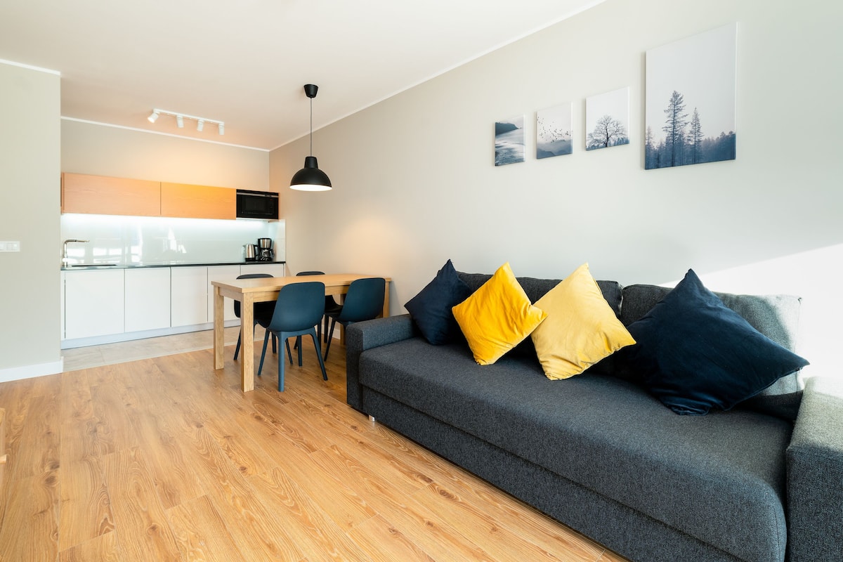 Una sala moderna con un sofá gris, una mesa de comedor de madera y sillas.