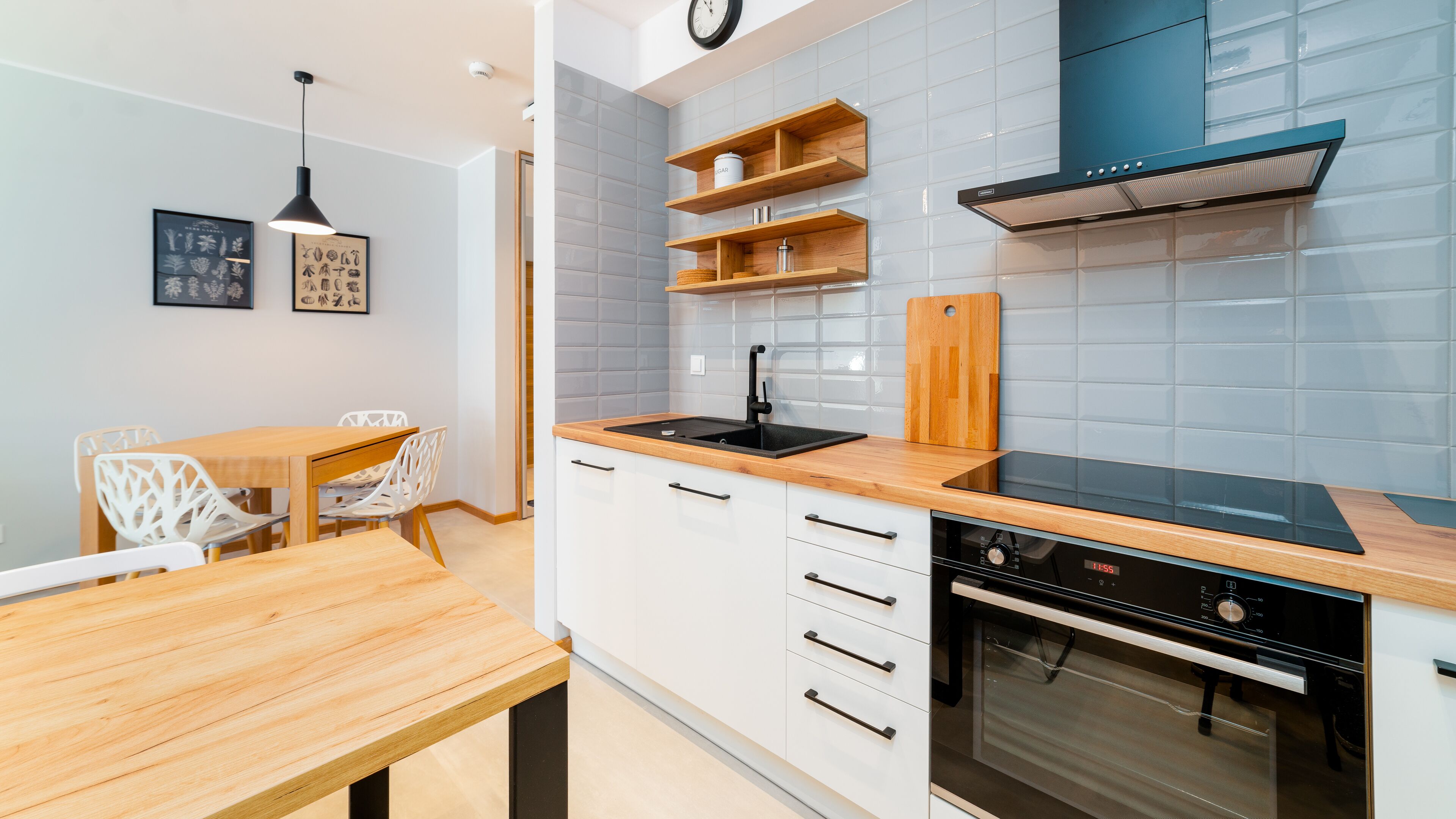 A modern kitchen with white cabinets, a wooden countertop, a black stove, and a blue range hood.