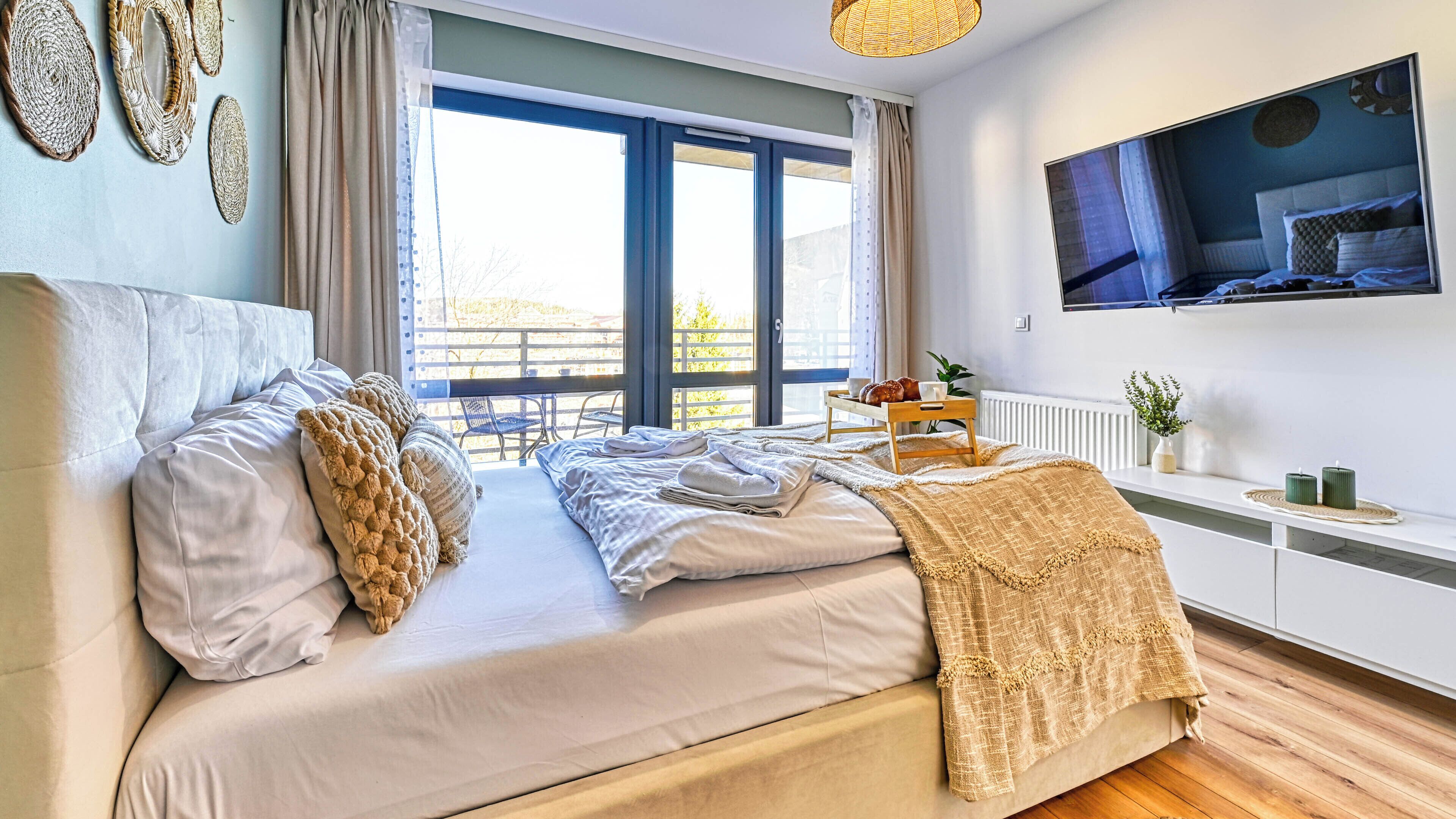 A bedroom with a bed, a TV mounted on the wall, and a window with curtains.