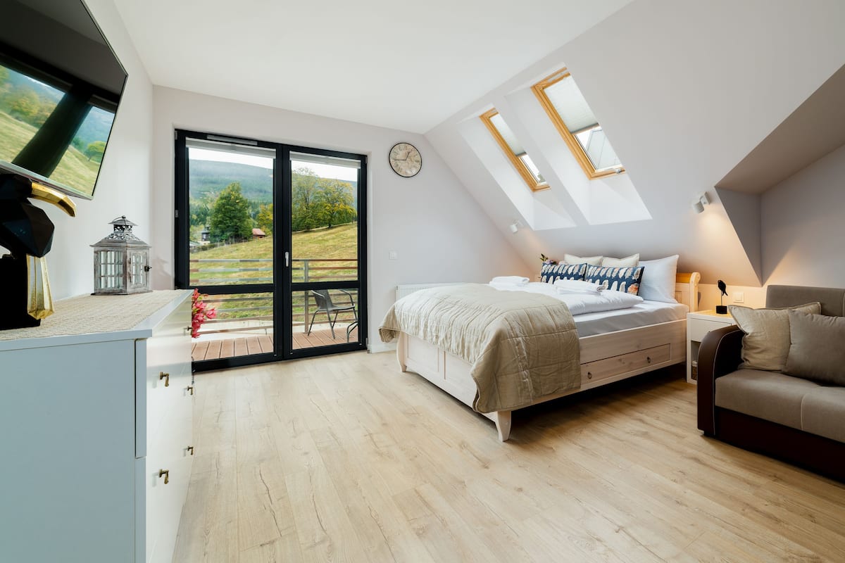Un dormitorio moderno con una cama grande, un sofá, un escritorio y vistas al exterior a través de una puerta corredera.