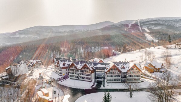 Un complejo turístico con varias construcciones tipo chalé, un edificio central con un cartel y un paisaje montañoso nevado.
