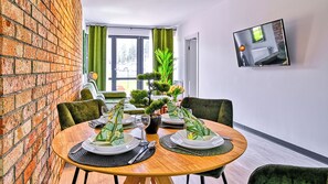 Comedor con pared de ladrillo, cortinas verdes, planta en maceta y televisor en la pared.