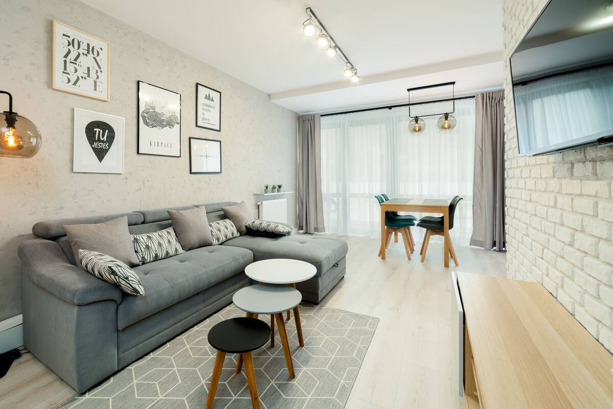 Una sala de estar moderna con un sofá gris, una mesa de centro redonda y una zona de comedor con una mesa y sillas.