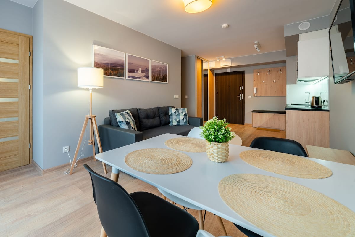 Una sala de estar moderna con un sofá, una mesa de comedor con individuales, una lámpara y una planta pequeña.