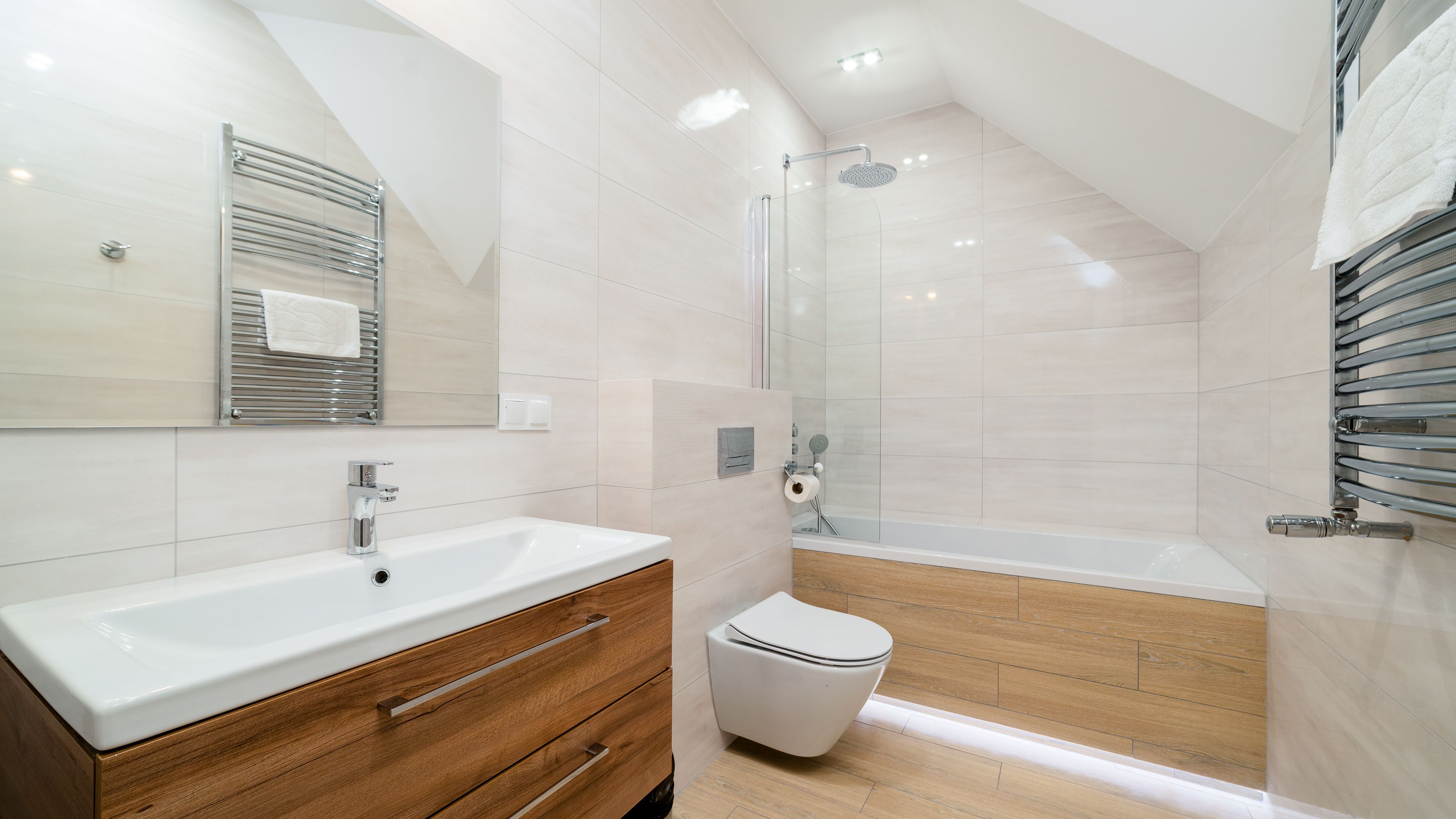 A modern bathroom with a white sink, wooden vanity, a glass shower enclosure, and a white toilet.