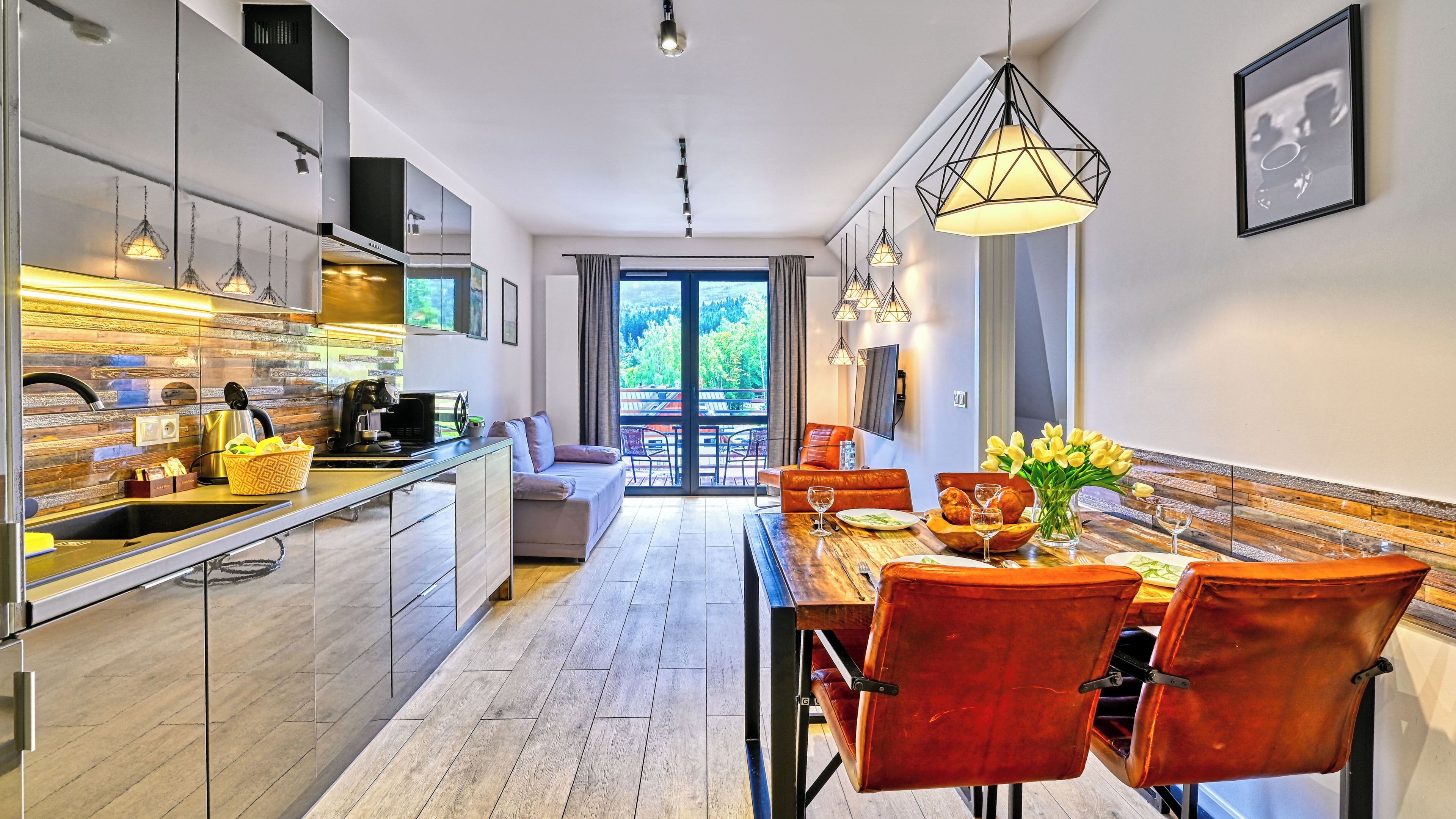 A modern kitchen with a dining area, wooden flooring, and a view to the outside.