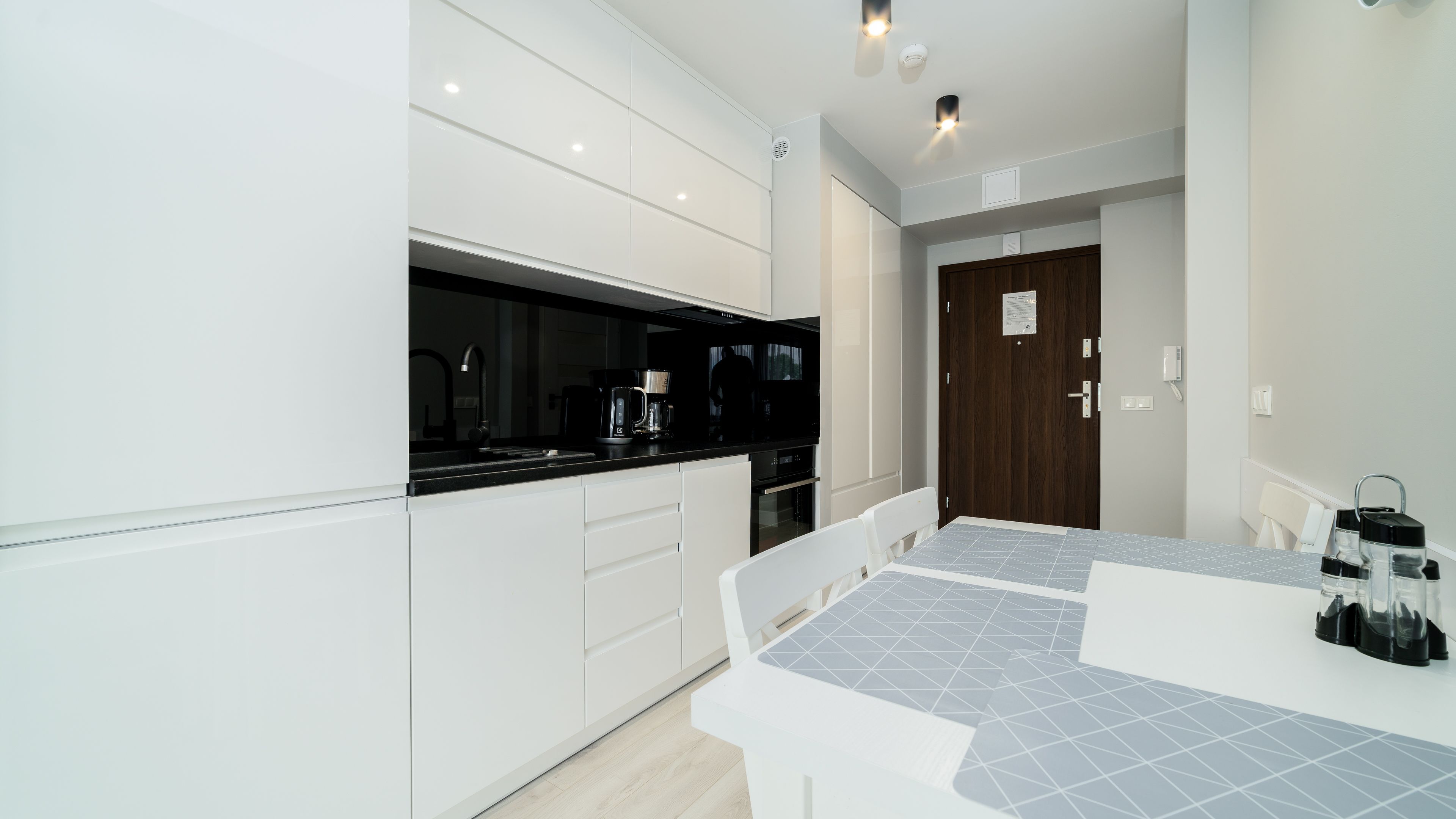 A modern kitchen with white cabinetry, a black countertop, and a tiled dining area.