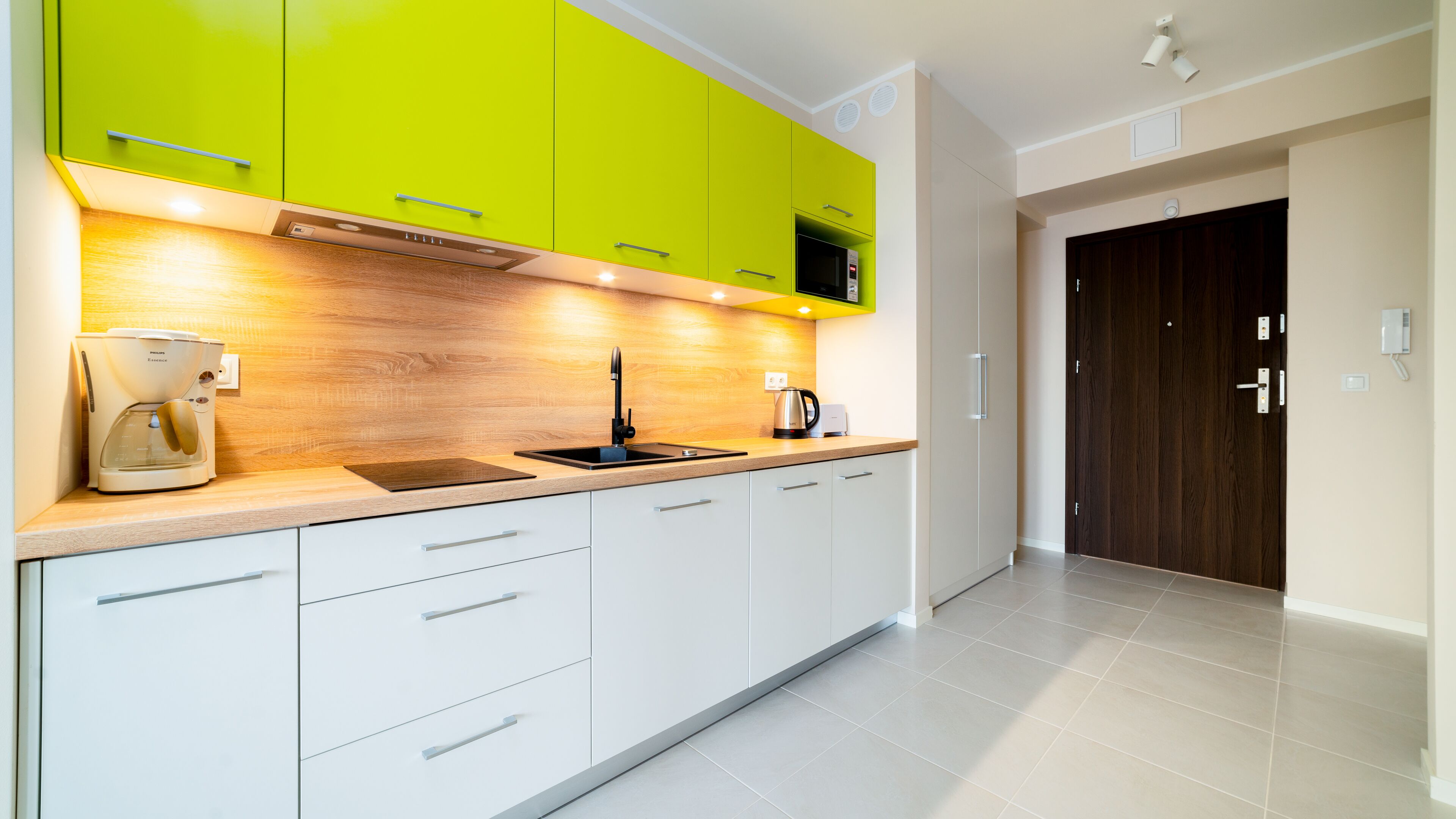 A modern kitchen with green cabinets, a coffee maker, and a kettle.