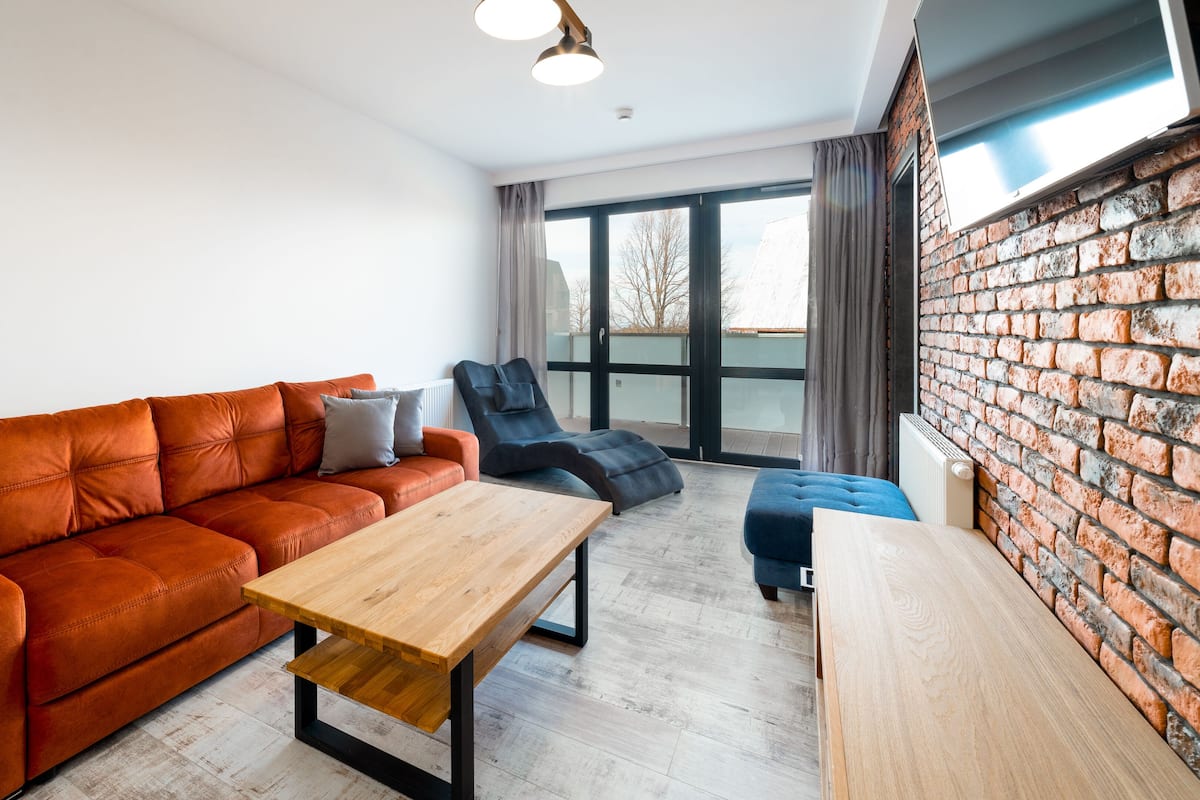 Una sala de estar moderna con un sofá, un sillón reclinable, una mesa de centro de madera y una pared de ladrillo.