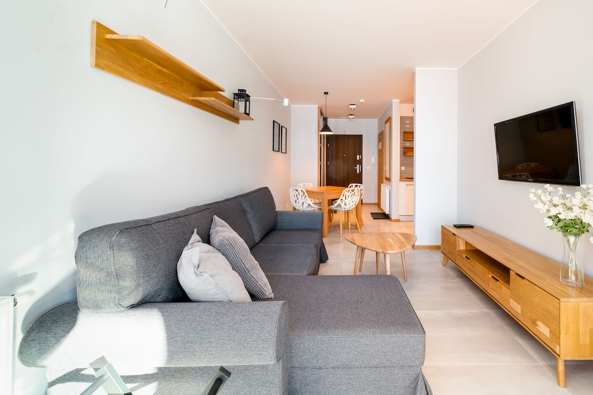 Una sala de estar moderna con un sofá seccional gris, un mueble bajo para televisor de madera y un comedor con mesa y sillas.