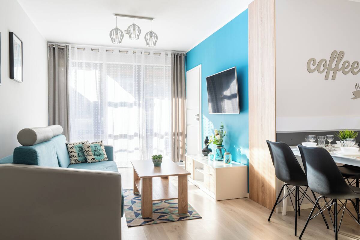 Una sala de estar moderna con un sofá, una mesa de comedor para dos personas y un cartel de café en la pared.