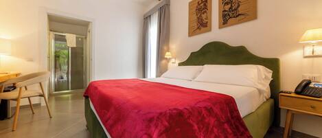 Habitación de hotel con cama, escritorio, silla, mesita de noche y teléfono en la pared.