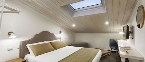 Une chambre avec un puits de lumière, un lit avec une tête de lit, des tables de chevet, un bureau avec une chaise et un miroir au mur.