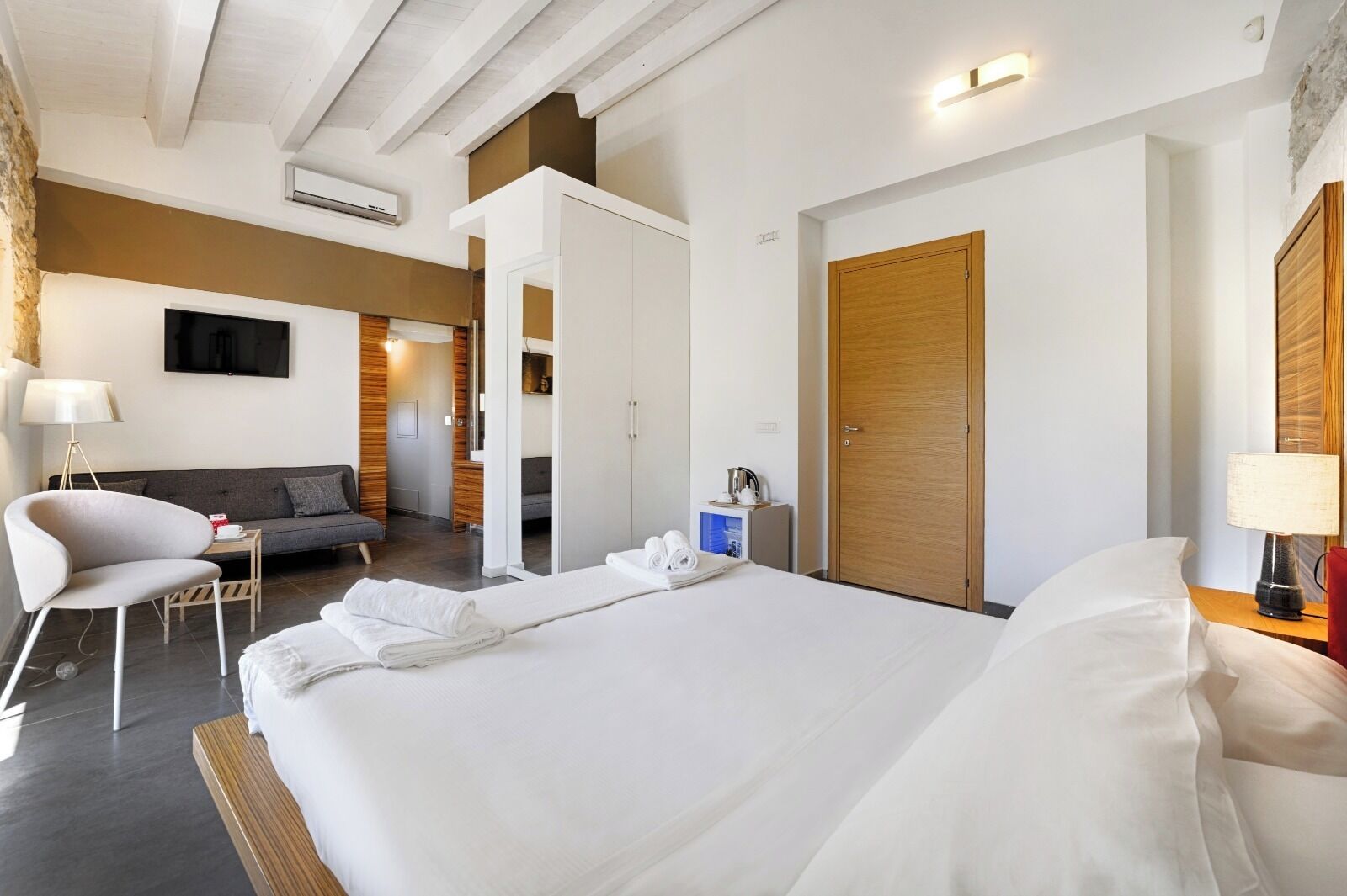 Una habitación de hotel con una cama grande, un sofá, una silla, un televisor y un armario de madera.