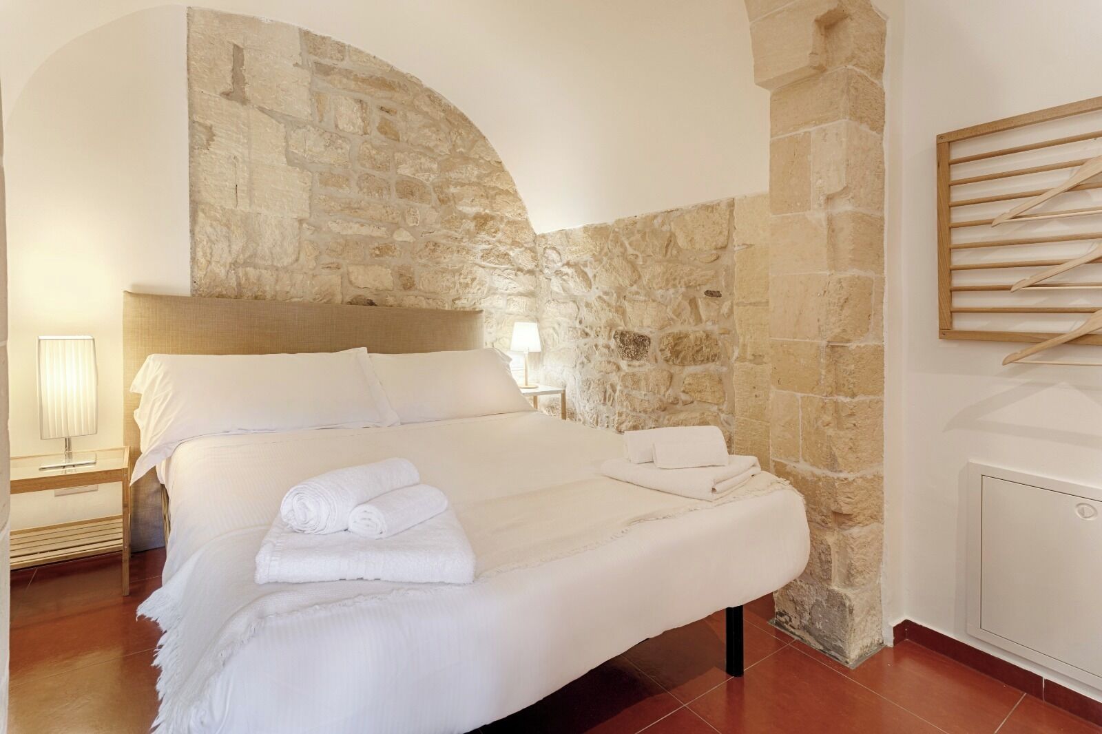 A bedroom with a stone wall, a bed with white linens, and a wooden headboard.
