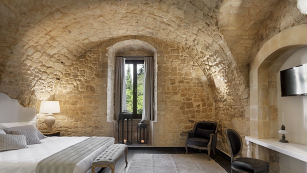 A bedroom with a stone arch, a bed, a desk, a chair, and a TV. - Itria Palace (Ragusa)