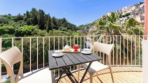 A balcony with a table set for tea, overlooking a hillside with buildings and greenery. - Itria Palace (Ragusa)