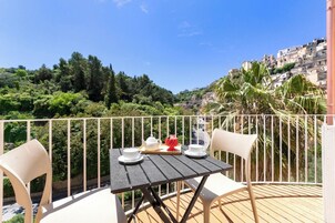 Un balcón con una mesa dispuesta para té, con vistas a una colina con edificios y vegetación.