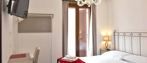 A hotel room with a bed, a desk, a chair, a TV, a chandelier, and an air conditioning unit.