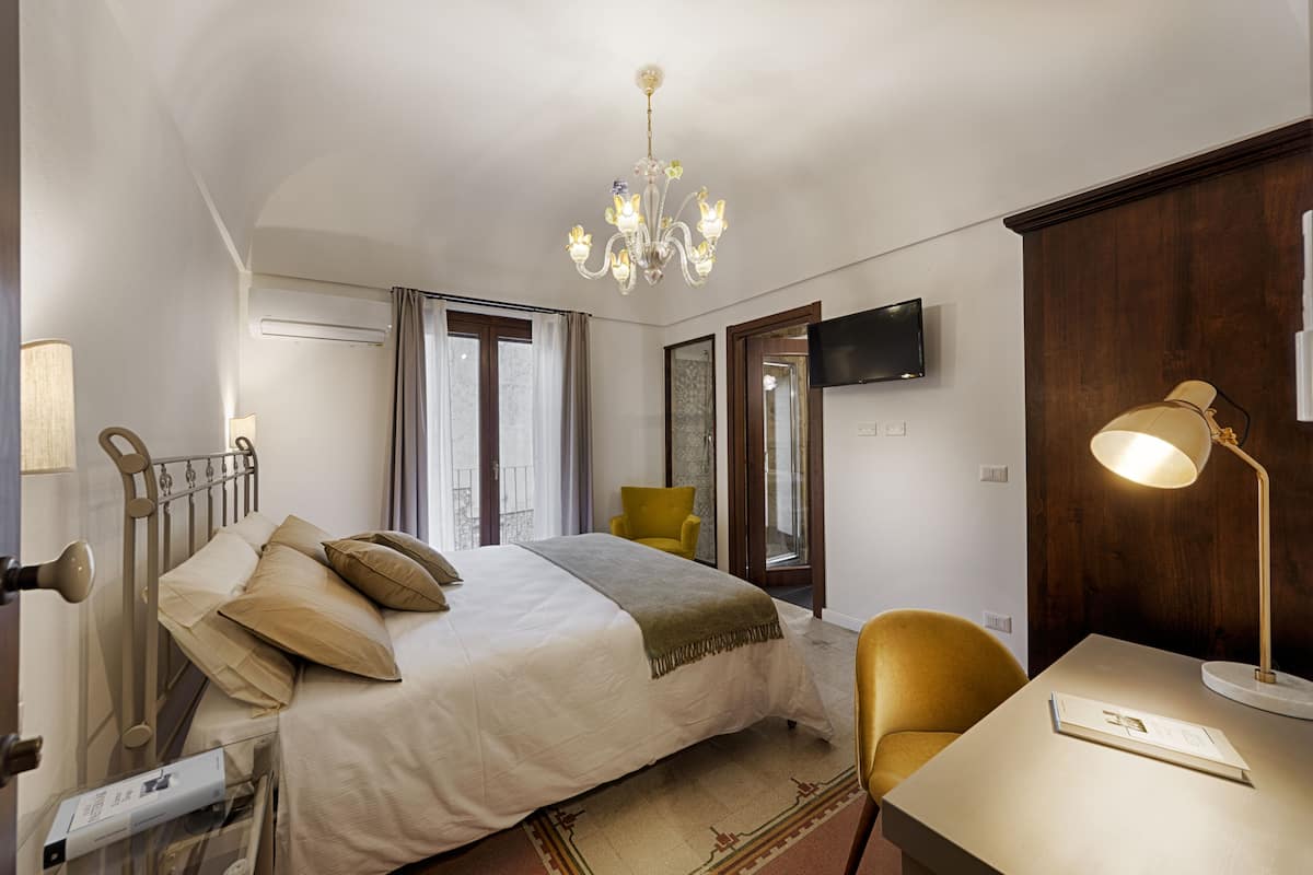 A hotel room with a bed, a desk, a chair, a television, and a chandelier.