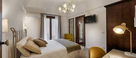 A hotel room with a bed, a desk, a chair, a television, and a chandelier.
